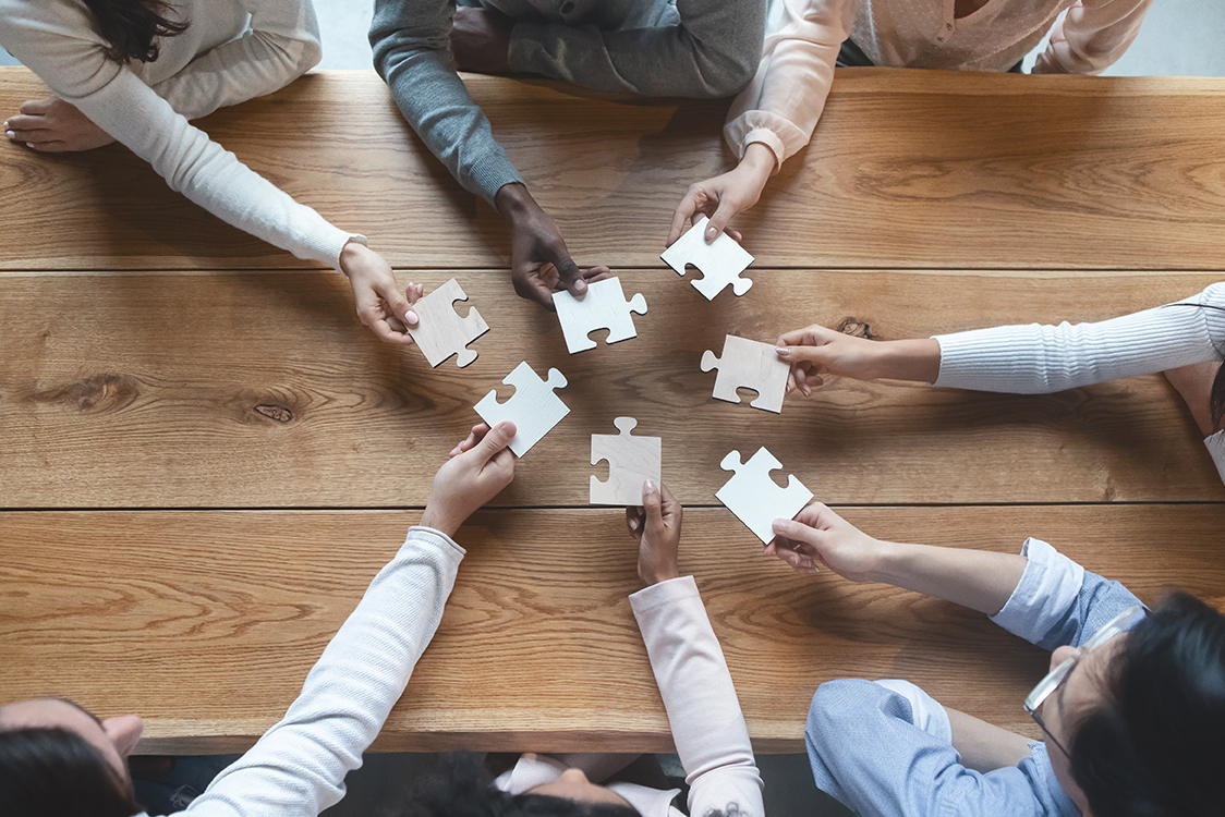 photo of people consulting around a table holding puzzle pieces.